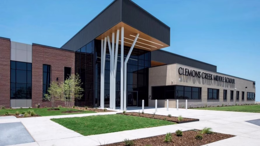 Modern middle school building with large glass windows, brick facade, and unique white pillar design, surrounded by greenery.