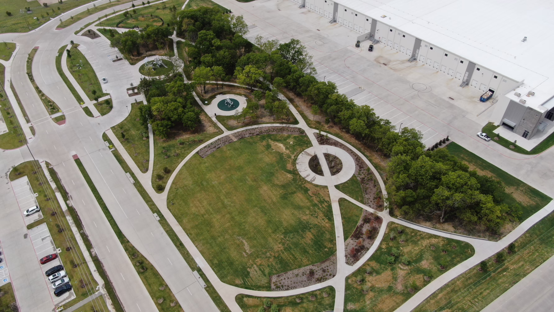 Aerial view of an industrial building with an adjacent landscaped park featuring pathways and greenery.