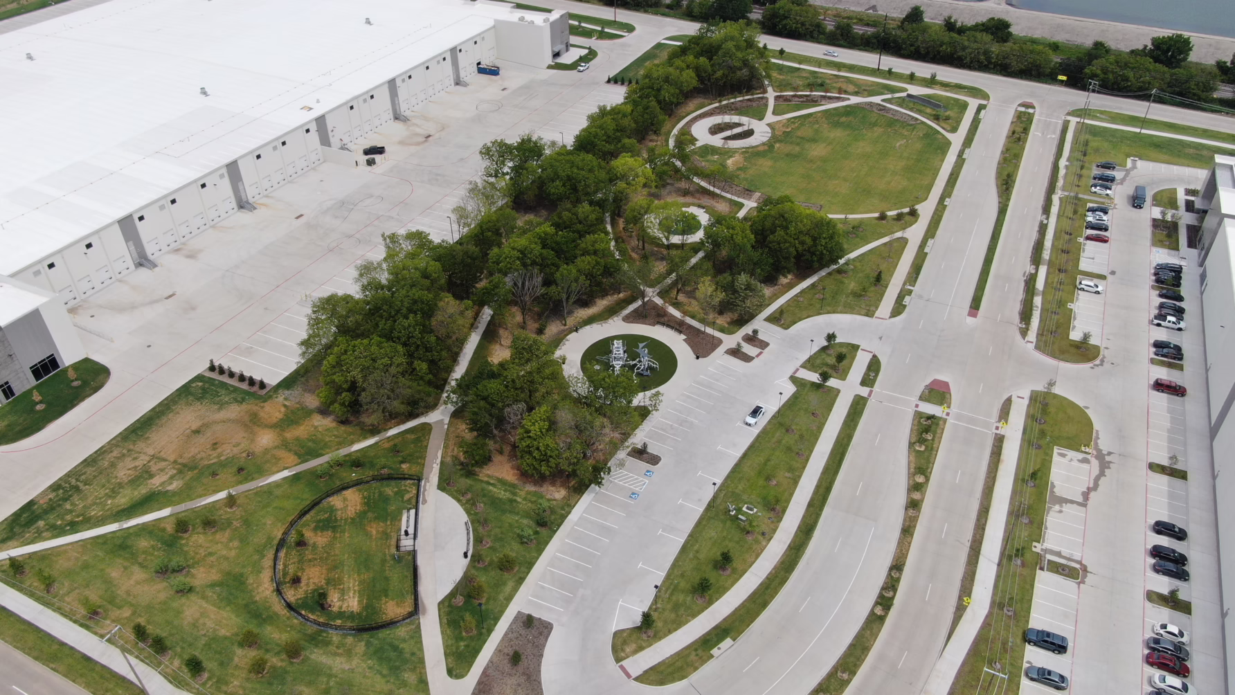 Aerial view of an industrial facility with parking lots, green lawns, and nearby water pond.