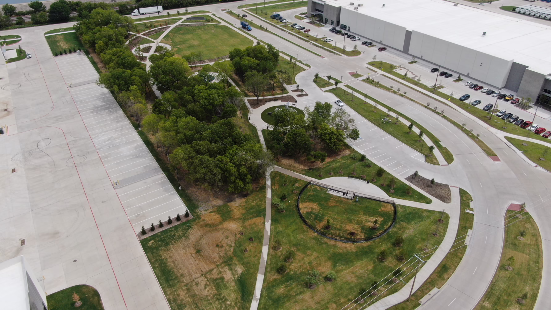 Aerial view of industrial park with large buildings, green spaces, parking lots, and access roads.