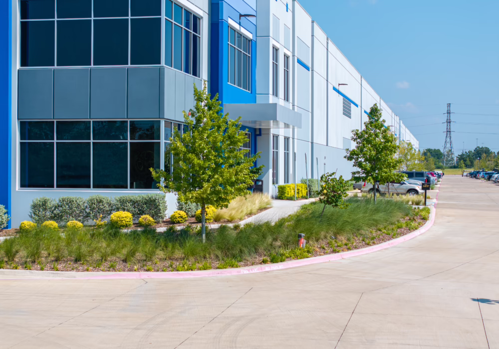 Modern commercial building with blue accents, large windows, and landscaped greenery on a sunny day.