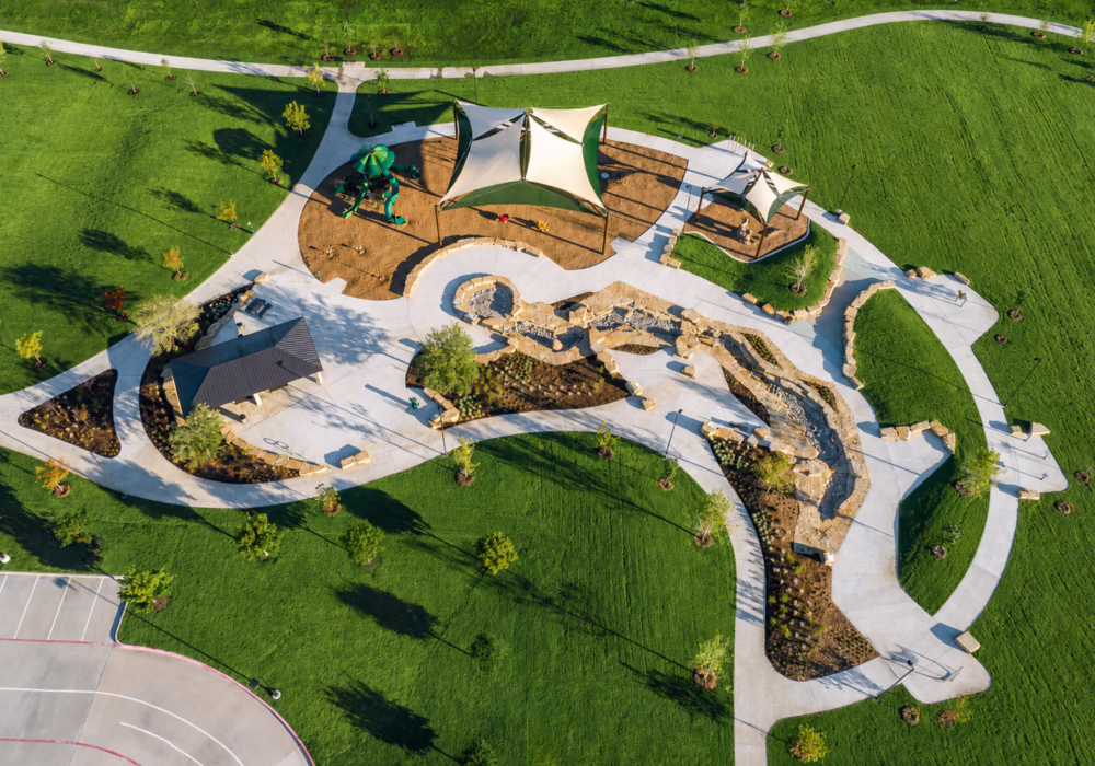 Aerial view of a landscaped park with pathways, playground, and green spaces on a sunny day.