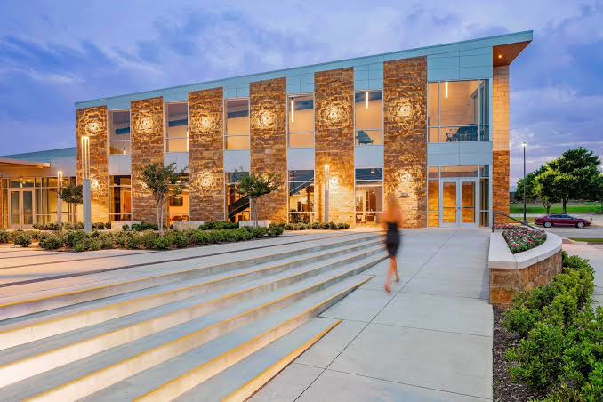 Modern building exterior with large glass windows and stone pillars, entrance steps, and a blurred figure approaching.