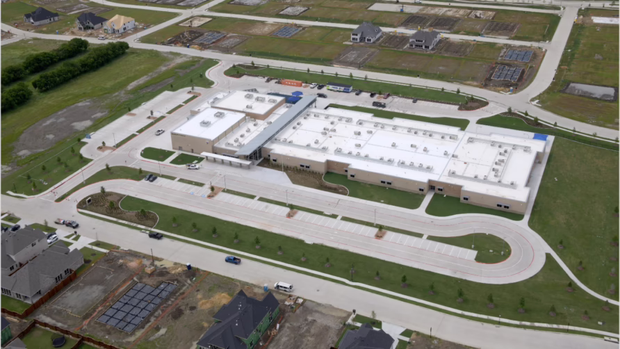 Aerial view of a modern school building surrounded by residential areas and roads.