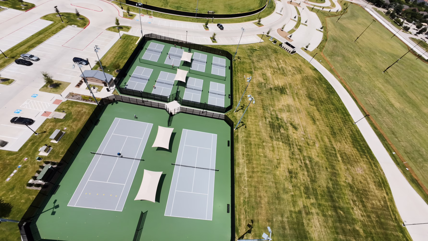 Aerial view of tennis courts and surrounding grass area in a sports complex.