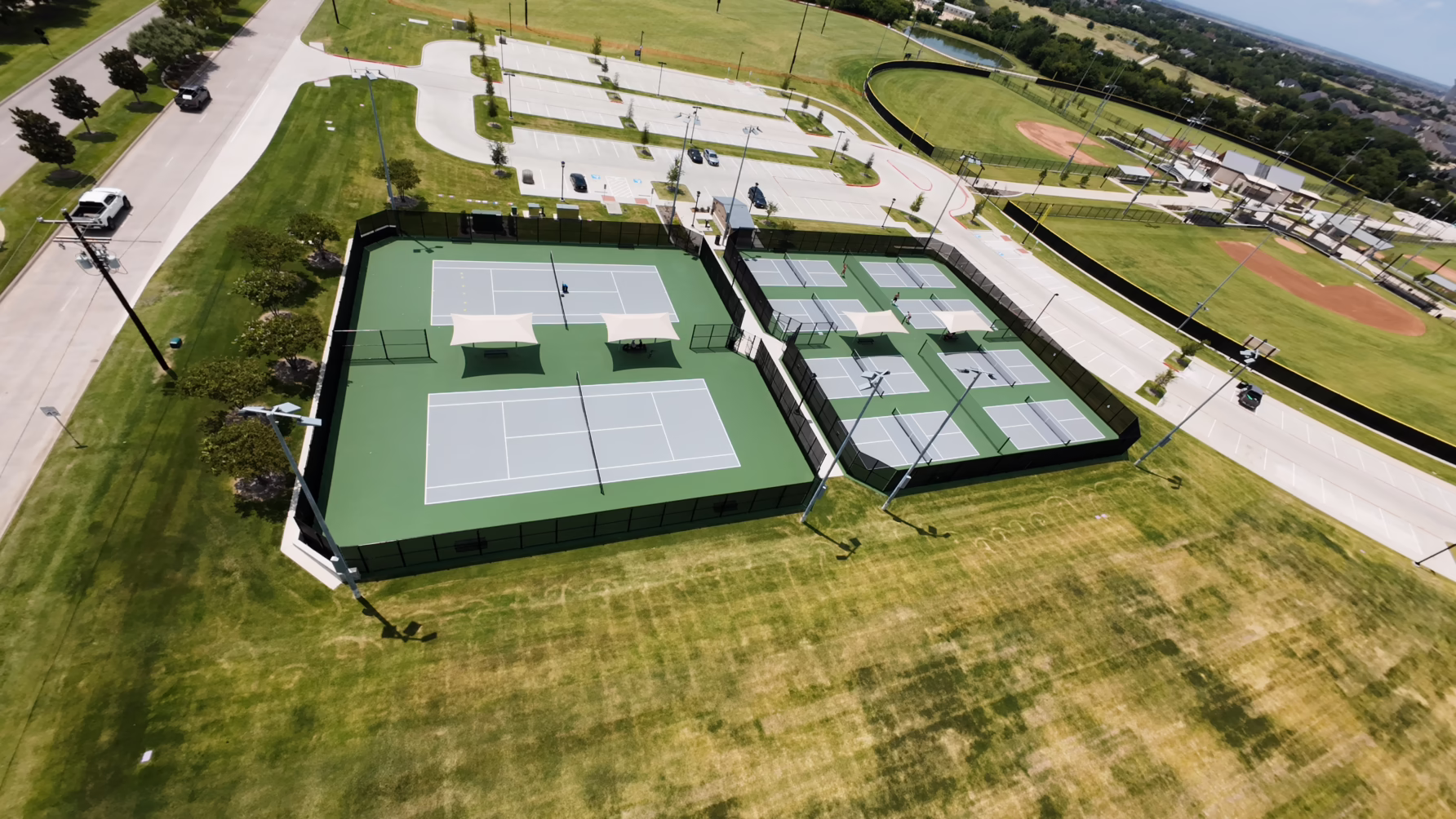 Aerial view of tennis and pickleball courts in a recreational park with parking and baseball fields nearby.